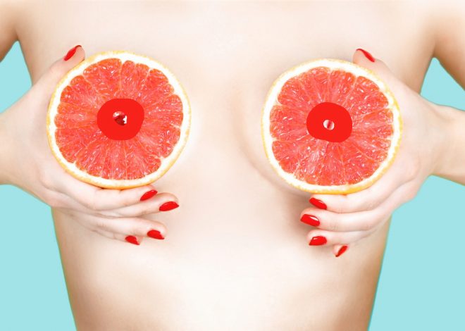 Sexy young woman holding grapefruits near her breasts on color background. Sexy young woman holding grapefruits near her breasts on color background. Erotic concept